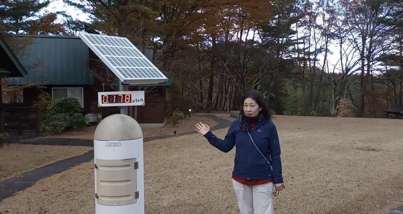 Woman stands next to radiation monitor