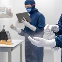 Medical facilty. Two people are in blue PPE with white gloves and one of them is spraying their hand.